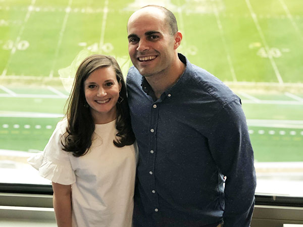 young man and woman standing together with a football field in the background